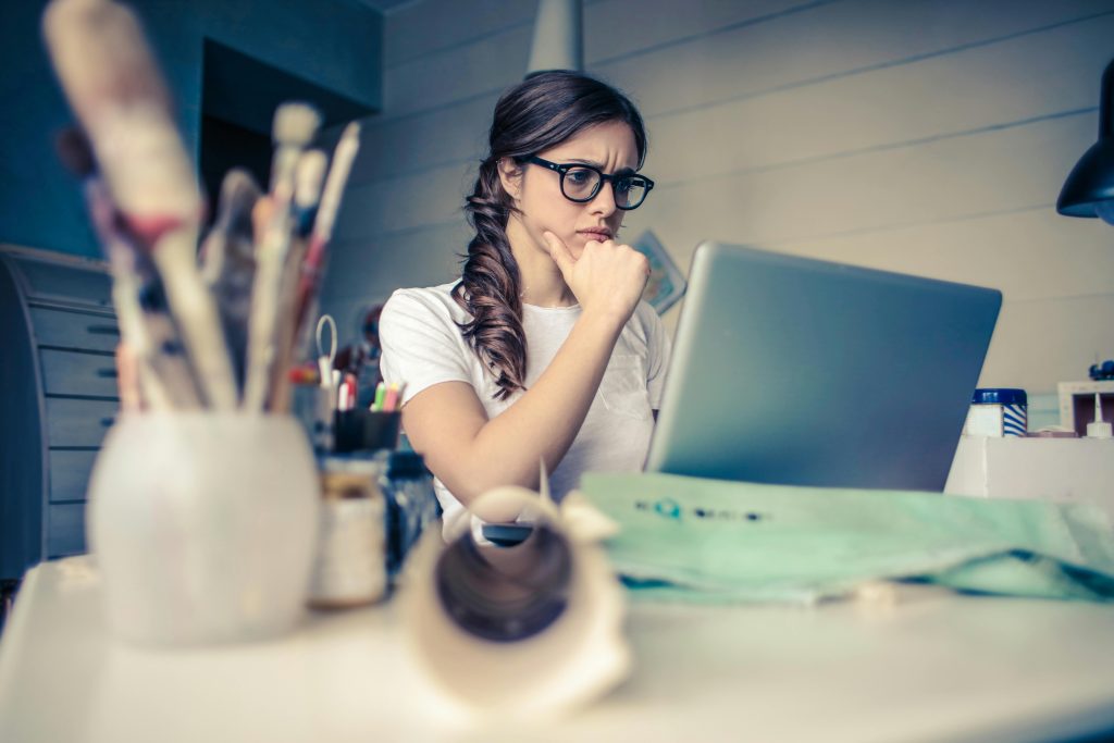 A woman sitting at a desk, looking worried as she stares at her laptop screen.