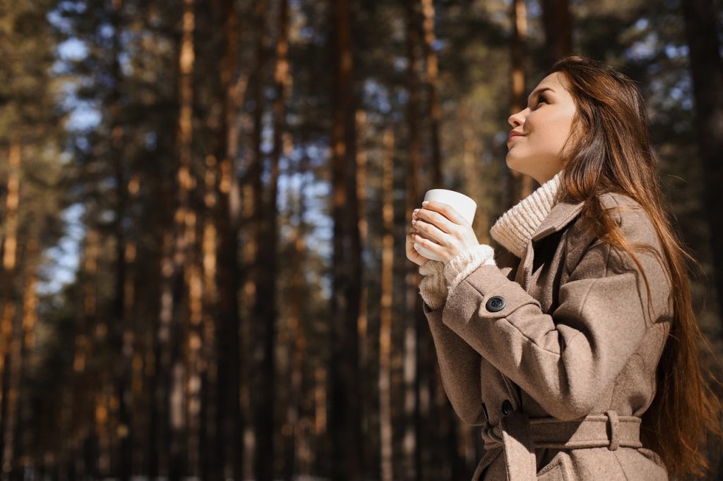 Woman outdoors drinking coffee, looking relaxed and content.