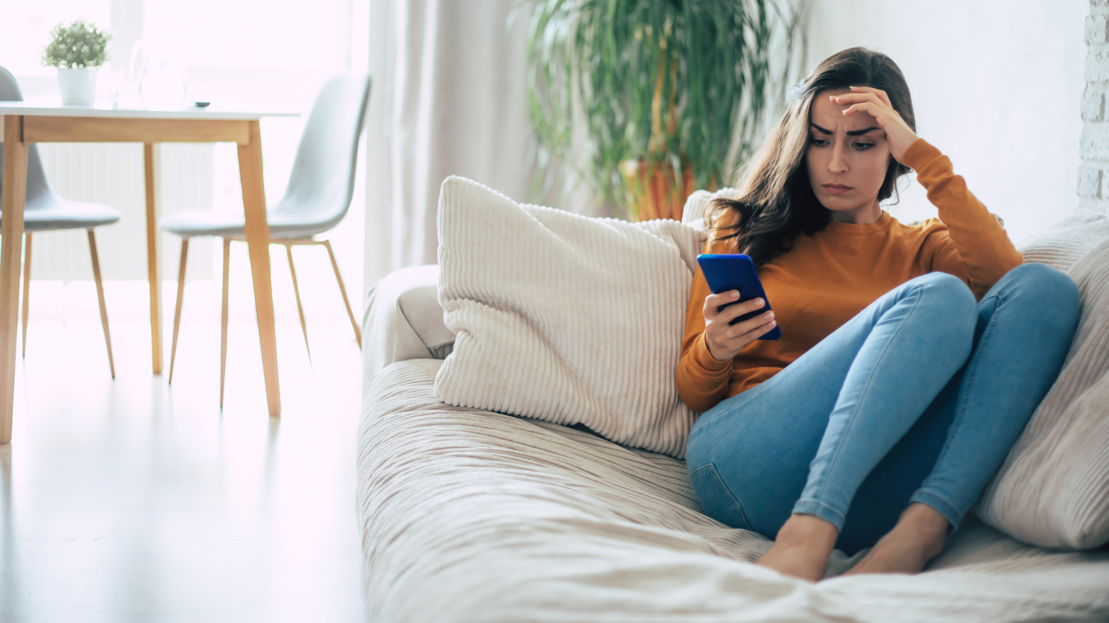 Stressed woman sitting on a couch, looking overwhelmed while texting on her phone.